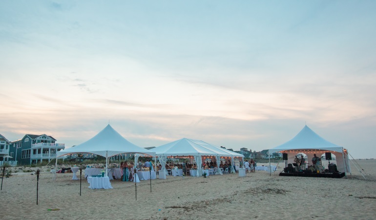 multiple white tents on the beach during the sunset