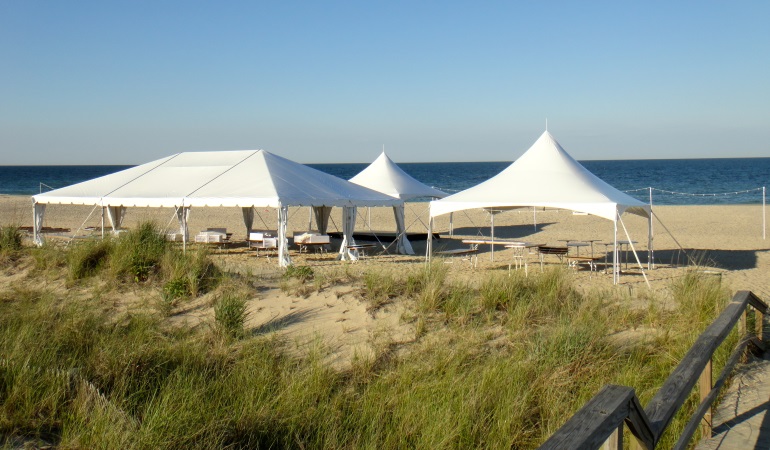 multiple white tents on the beach by the dunes
