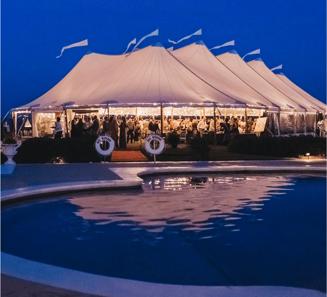 large white tent with white flags on top beside a pool
