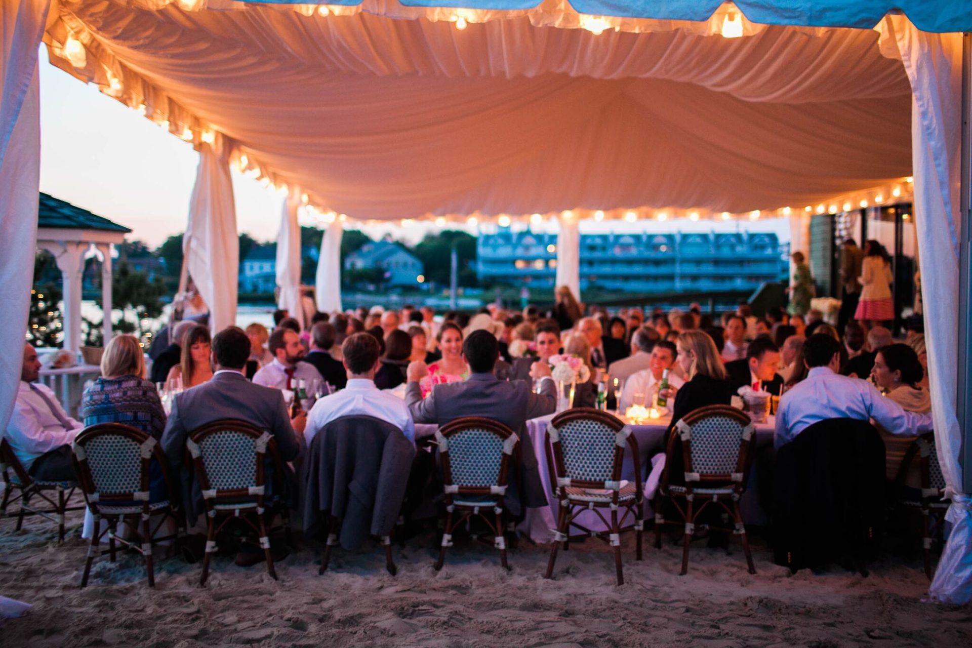 multiple tables of people eating under a white tent
