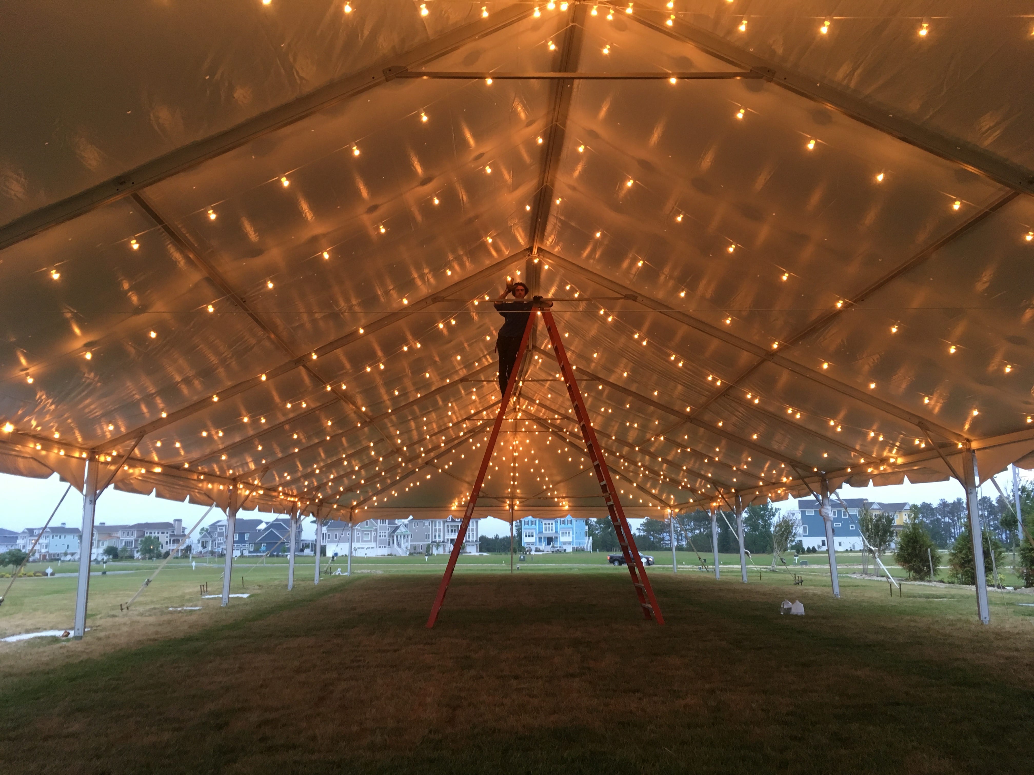 person on a ladder setting up string lights in a large white tent