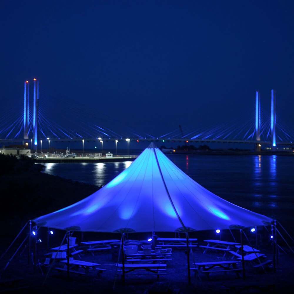 White tent with blue LED lights and bridge in the background