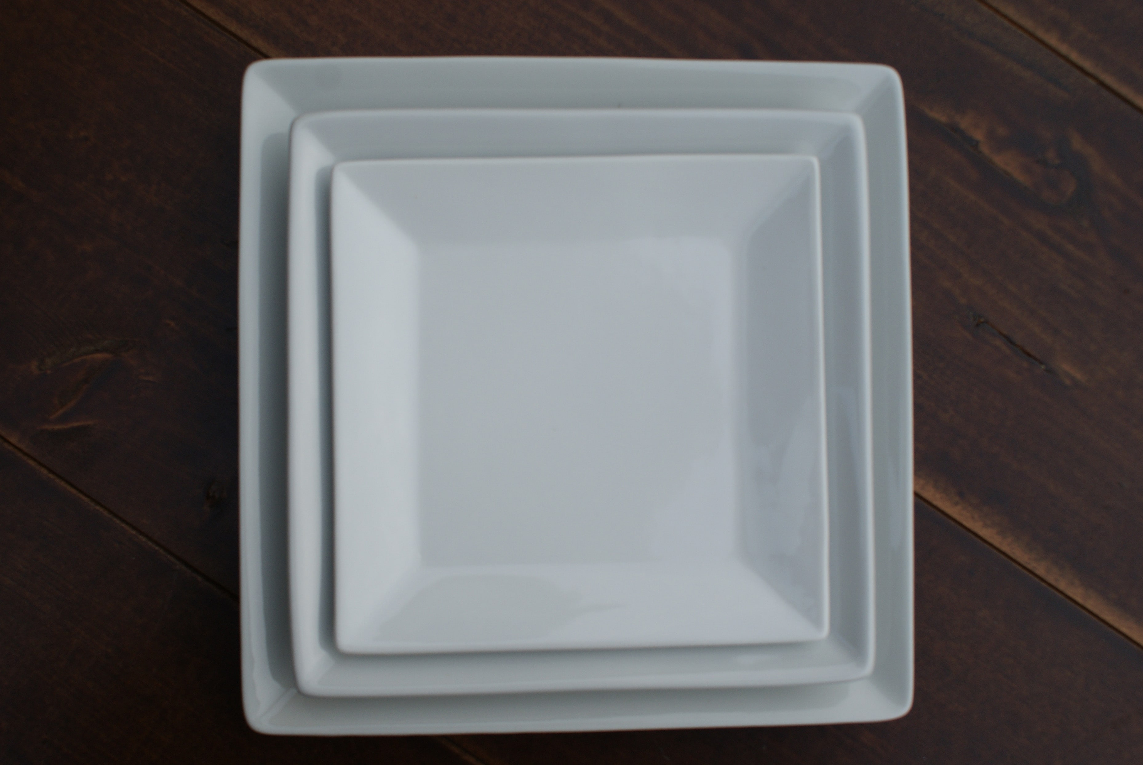 white square china plates stacked on a wood table