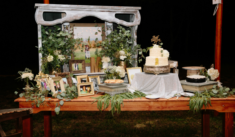 wooden farm table with plants and pictures next to a white wedding cake