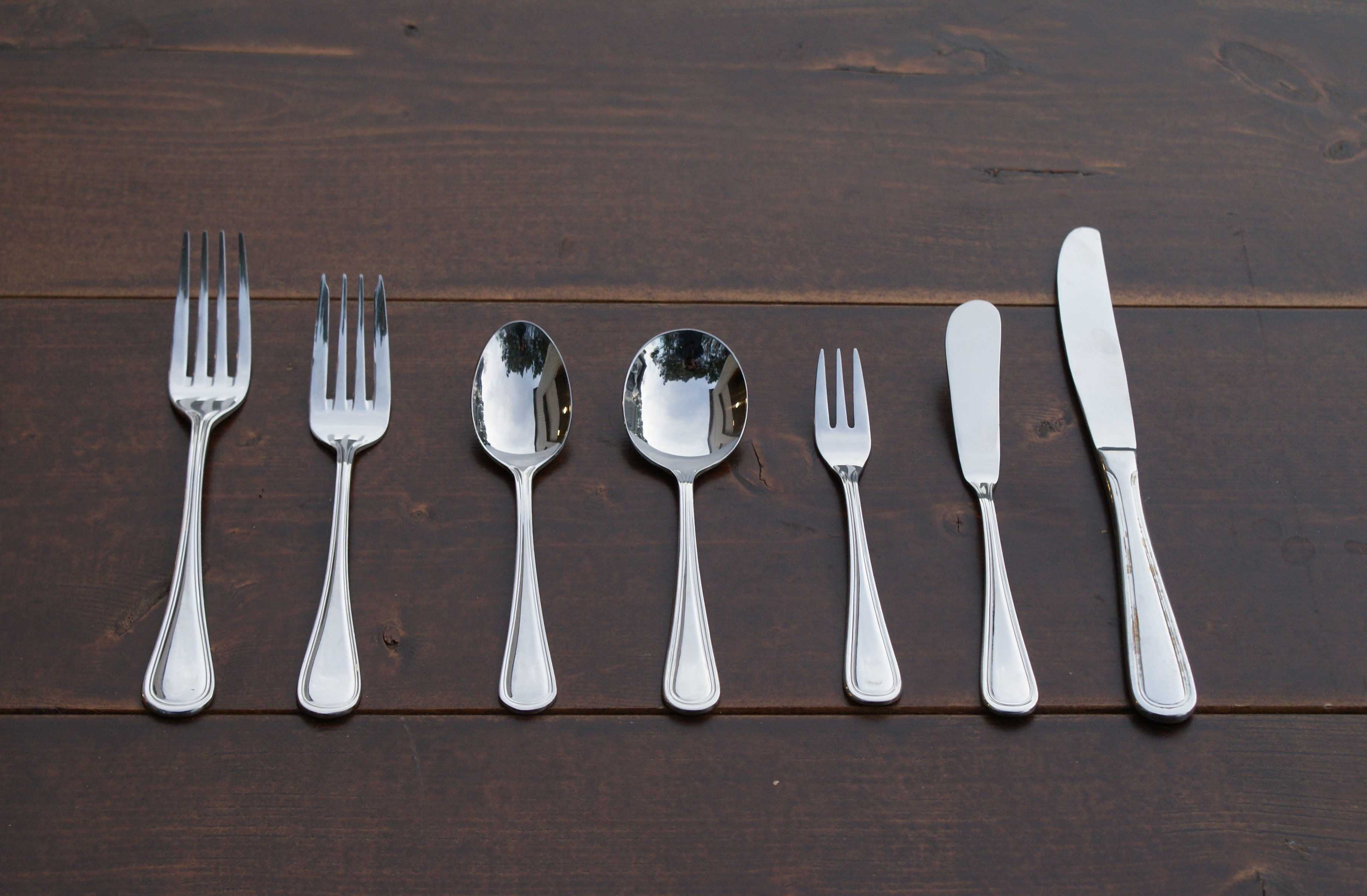 silver utensils lined up on a wood table