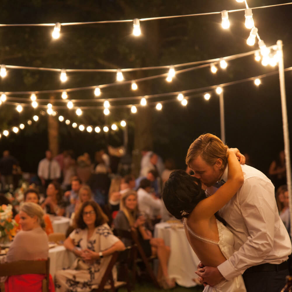 Bride and groom kissing under a string of lights in the vineyard
