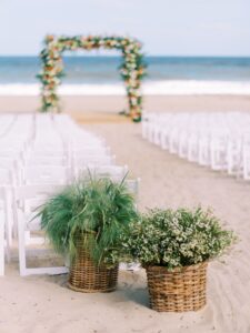Picture of wedding on the beach with chairs and florals.