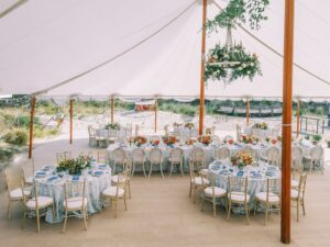 Picture of tables and chairs inside the wedding tent with florals and table settings.